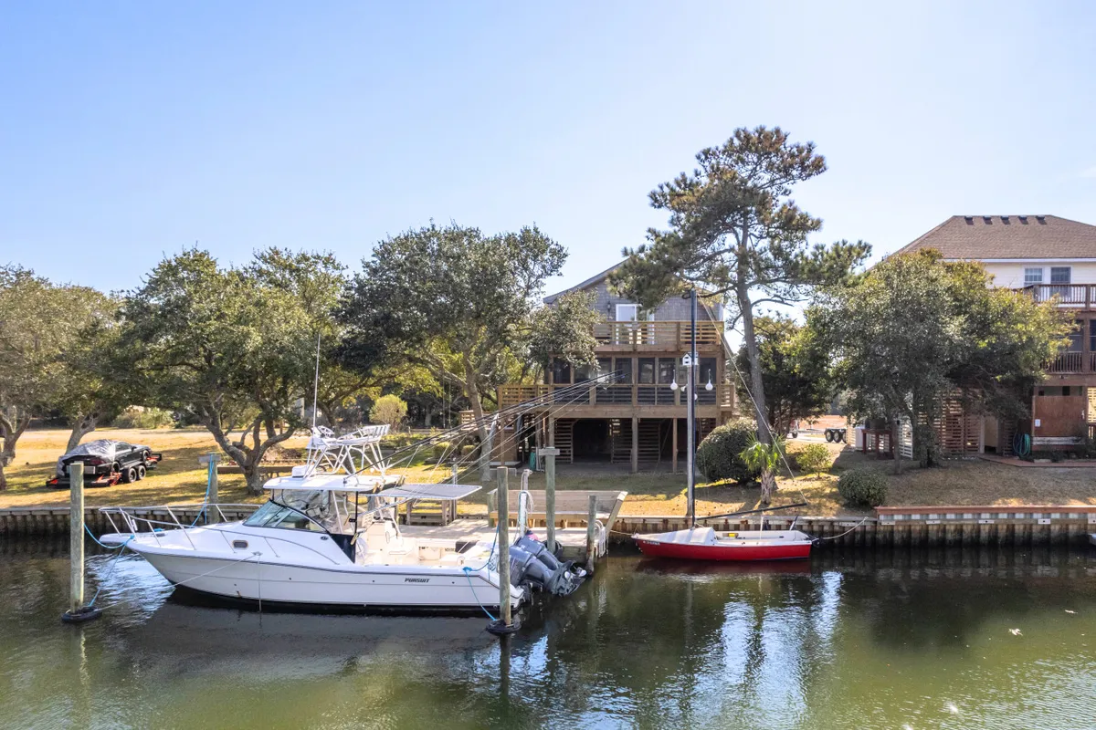 This image showcases boats moored at a private dock adjacent to a wooden deck, with trees surrounding the water's edge. The tranquil water reflects the setting sun, and the deck appears perfect for morning coffee or evening relaxation.
