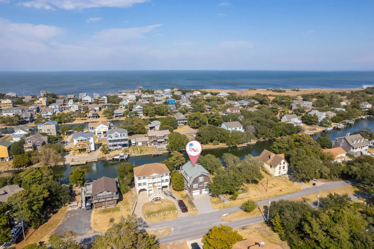 This exterior view highlights the house with a palm tree icon, showing its prime location along a canal within a quiet neighborhood. The canal runs through the area with an ocean view visible in the distance, emphasizing easy access to both waterways and beaches. The image conveys tranquil surroundings ideal for family strolls or outdoor play.