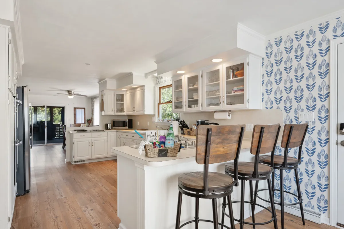 A modern, inviting kitchen is showcased with a central island, bar stools, a decorative backsplash, and a large window that brings in natural light. The space is set up for cooking, entertaining, and casual dining.