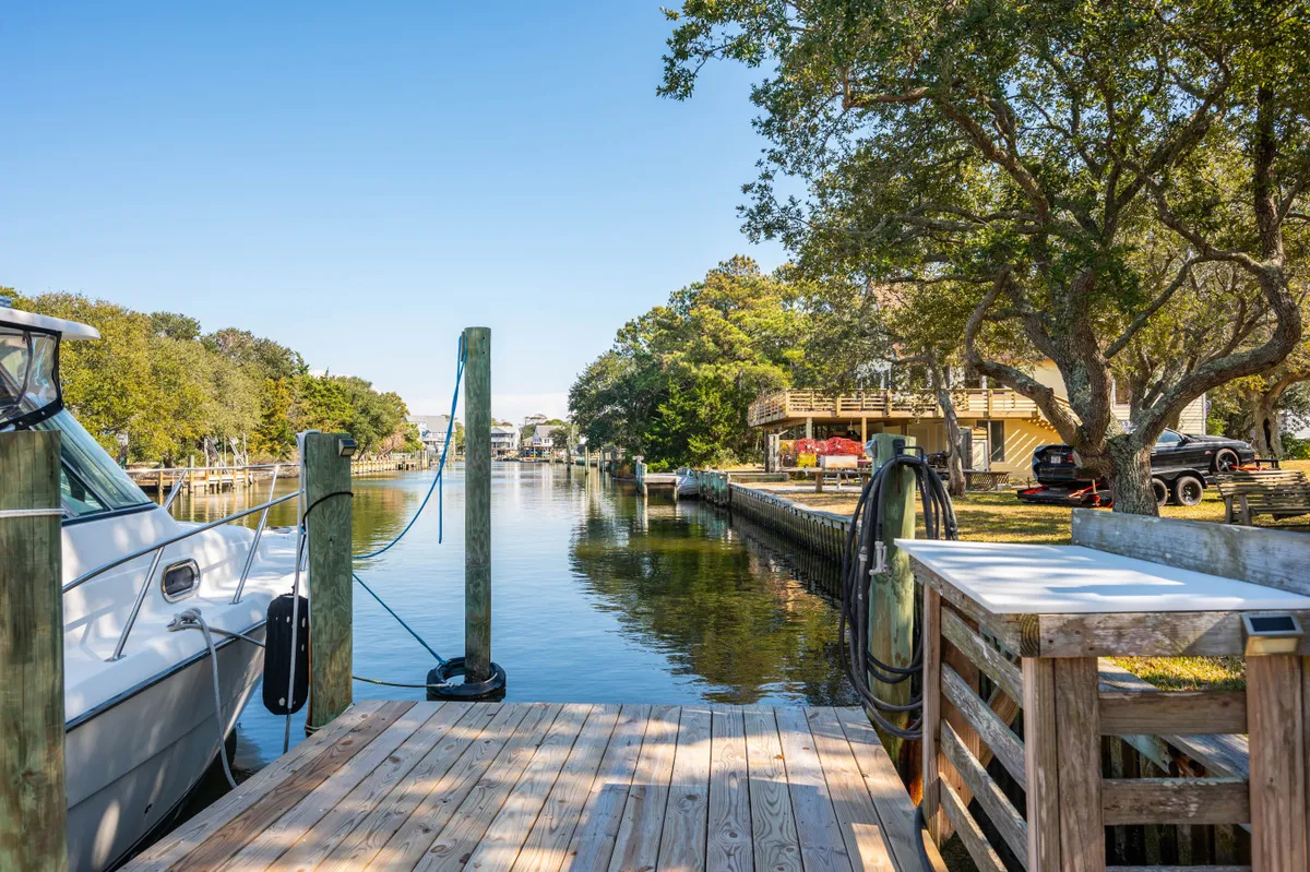 A peaceful canal scene featuring a dock, boats, and the surrounding lush greenery and waterfront homes. The dock invites fishing or launching kayaks, with the calm water reflecting the sky at sunset.