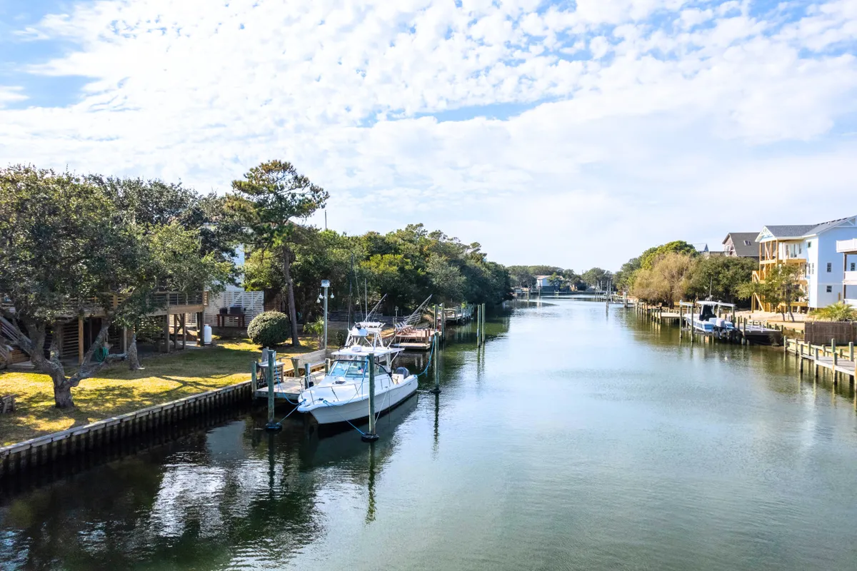 The hero image showcases peaceful boats moored along a tranquil canal lined with lush greenery, under a wide, clear blue sky dotted with soft clouds. The scene evokes a sense of serenity and connection to nature, inviting activities like boating, fishing, and leisurely strolls along the water's edge. The image captures the magic of canal-front living, with opportunities for sunset boat rides and morning adventures just steps from the home.