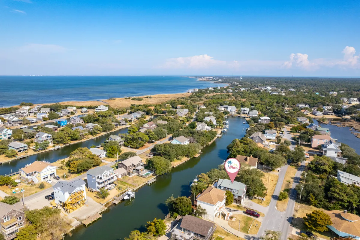 A sweeping aerial view of the waterways, lush marshlands, and nearby houses, with the ocean visible in the distance and roads winding through the landscape. The scene feels peaceful, highlighting the natural environment and sense of being surrounded by water and greenery.