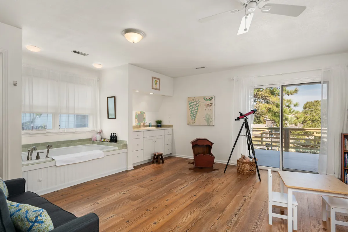 A cozy interior scene featuring a telescope by a sliding glass door, a bathtub, and artwork on the wall. The telescope hints at stargazing opportunities, while the view outside suggests a close connection to the outdoors.