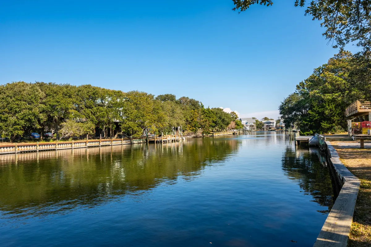A serene view of calm canal waters bordered by lush greenery and a boardwalk path, evoking peaceful moments spent outdoors. The tranquil atmosphere sets the scene for morning strolls, sunset watching, or a quick break to connect with nature.