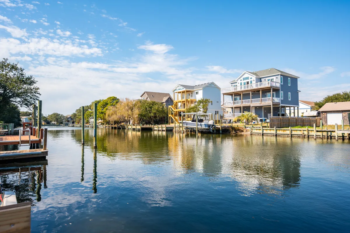 A tranquil waterfront scene featuring reflections of neighboring houses and docks on the still water. The setting suggests a place to relax, enjoy breakfast on the porch, or launch a paddle for a midday escape.