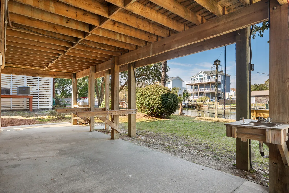 A casual outdoor space with wooden beams overlooking the canal, an outdoor workbench perfect for prepping fishing gear or cleaning the day's catch, and landscaped greenery. The scene hints at gatherings and relaxed waterfront barbecues.